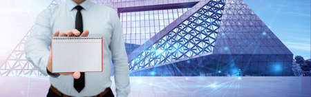 Man Wearing Black Tie Holding Empty Page Graphing Notebook Around Futuristic Technology. Employee Presenting Blank Workbook Surrounded By Modern Automation.の写真素材