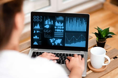 Woman Typing On Laptop Beside Coffe Mug And Beautiful Plant Accomplishing Work From Home. Girl Encoding Minicomputer Next To Cap And Flower Finishing Remote Jobs.の写真素材