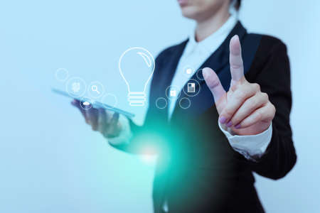 Woman In Suit Side Standing Holding Tablet While Raising Finger Showing Futuristic Interface. Lady In Uniform Carrying Mobile Phone Pointing On Modern Graphic Display.の写真素材
