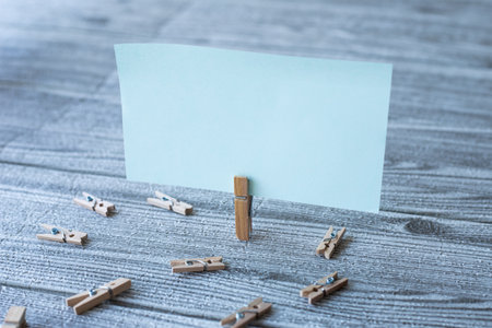 Piece Of Blank Square Note Surrounded By Laundry Clips Showing New Meaning. Empty Sticky Paper Clipped Upright Placed On Top Of Wooden Table Displaying Fresh Idea.の写真素材