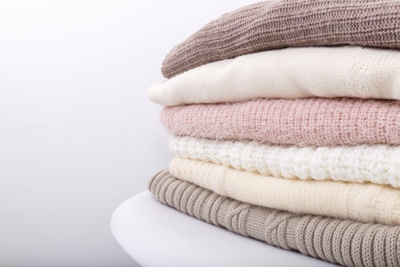 Stack of cozy knitted sweaters or blankets pastel trending colors on white modern chair against the...