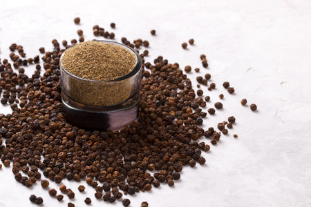 Black pepper corns and powder on white stone background, top view with copy space