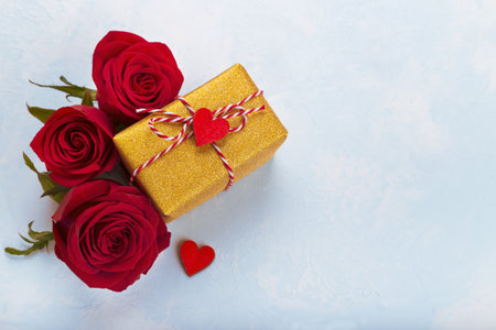 Red roses and golden gift box with ribbon on blue background cope spaceの写真素材