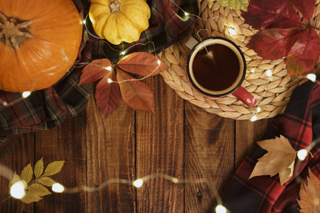 Hot cup of tea blanket pumpkins autumn leaves and fairy lights on old wooden background Vintage seasonal relax conceptの写真素材