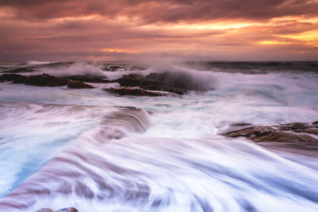 Large waves wash into the tidal ocean pool at sunrise