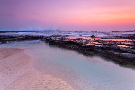Pretty sunrise over the beach and rock shelf with reflectionsの写真素材