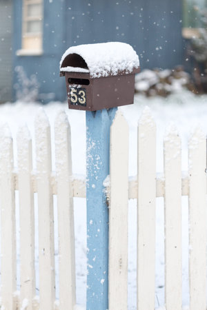 Mailbox and picket fence with falling snow in winter