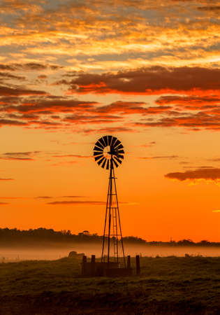 Windmill and misty morning across rural farmland fieldsの写真素材