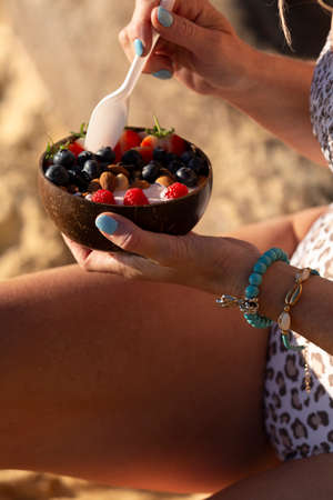 Woman eating a healthy breakfast from a coconut bowl on beachの写真素材