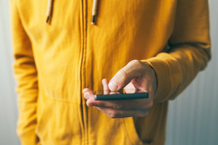 Young man in yellow shirt using smartphone, close up of hand with selective focusの写真素材