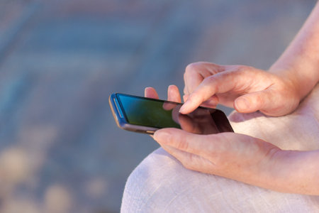 Close up of caucasian female hands using mobile phone outdoors, selective focusの写真素材