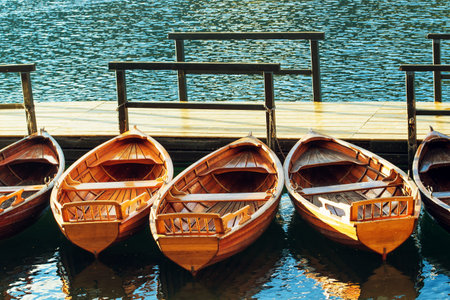 Small wooden boats docked and tied to empty pier on the lake