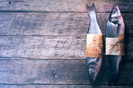 Two raw bass fish on wooden background with blank space
