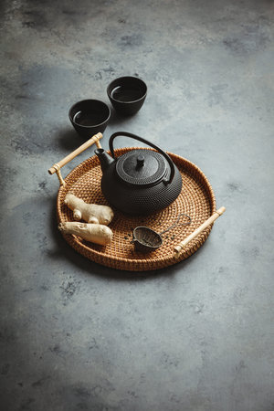 Traditional Asian tea ceremony arrangement. Iron teapot, cups, dried green tea leaves, ginger and...