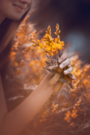 Dreamy photo of a nice girl enjoying aroma of a little yellow wildflowers, spending beautiful spring day on the floral field, enjoying life, freedom conceptの写真素材