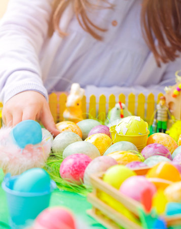 Closeup photo of a little girl's hand painting many colorful eggs, traditional Easter symbol, the...