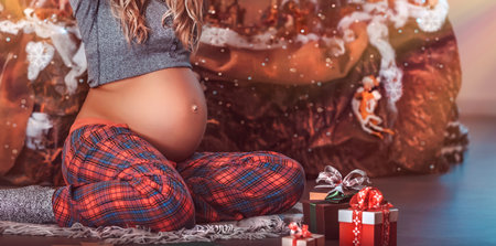 Happy pregnant woman at Christmas eve sitting on the floor in the decorated room at home and preparing to open Christmas gifts, new life as the best present for Xmas holidaysの写真素材