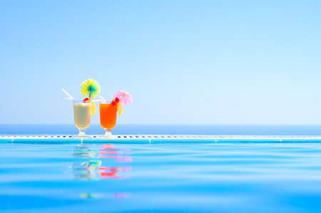 Two Colourful Tropical Cocktails near the Swimming Pool on the Background of Warm Blue Sea. Exotic Summer Vacation.の写真素材