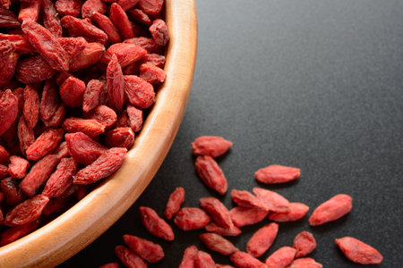 Wooden Bowl Full of Dried Goji Berries on the Black Table. Healthy Dietの写真素材