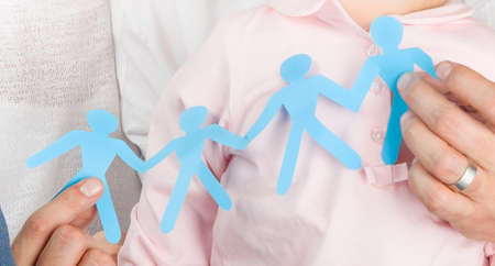 Man's hands holding a blue paper cut group of people, conceptual photo of standing together, teamwork, friendship, and family support..の写真素材