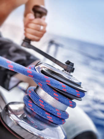 Holder of rope on sailboat, man pulling handle of spool, macro photo of yacht detail, working on water transport, luxury summer time sportの写真素材