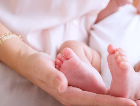 Mother hand holding cute tiny baby feet, doing massage for little newborn child, happy motherhood, protection and safety conceptの写真素材