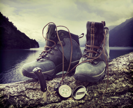 Hiking boots with compass on tree trunk near lakeの写真素材