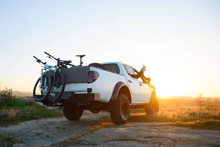 Friends Driving the Pickup Offroad Truck in the Mountains with Bikes in the Body at Warm Autumn Sunset. MTB Adventure and Car Travel Concept.の写真素材