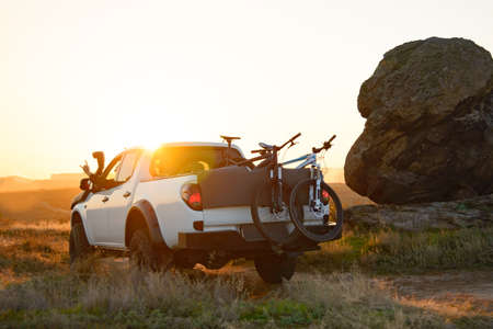 Friends Driving the Pickup Offroad Truck in the Mountains with Bikes in the Body at Warm Autumn Sunset. MTB Adventure and Car Travel Concept.の写真素材