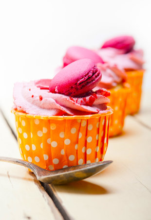 fresh pink berry cream cupcake with macaroon on top over rustic wood table
