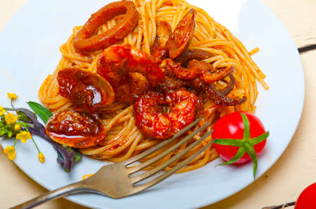 Italian seafood spaghetti pasta on red tomato sauce over white rustic wood tableの写真素材