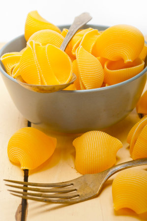 raw Italian snail lumaconi pasta on a blue bowl over rustic table macro