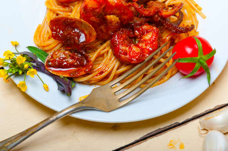 Italian seafood spaghetti pasta on red tomato sauce over white rustic wood tableの写真素材