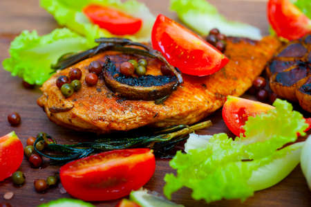 wood fired hoven cooked chicken breast on wood board with herbs spices and vegetablesの写真素材