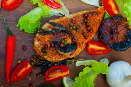 wood fired hoven cooked chicken breast on wood board with herbs spices and vegetables