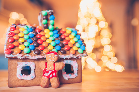 Gingerbread fairy house on a background of bright Christmas tree with garlandの写真素材