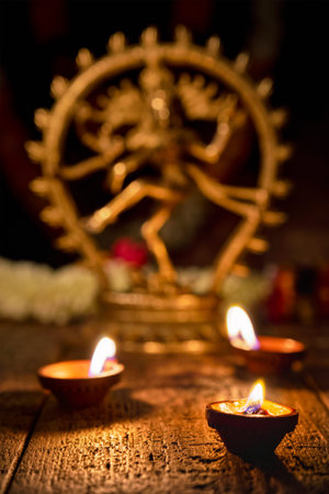 Maha Shivaratri or Diwali concept - Shiva Nataraja statuette with Diwali lights oil ghee candles,...
