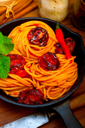 italian spaghetti pasta and tomato with mint leaves on iron skillet over wood boardの写真素材