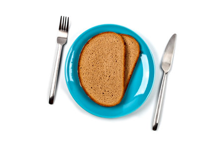 Fresh baked bread slices on blue plate, fork and knife on white background. Top view image.