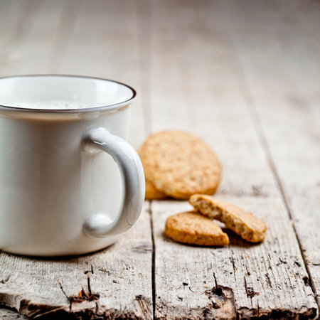 Cup of fresh milk and some homemade baked oat cookies on rustic wooden table background. With copy space.の写真素材