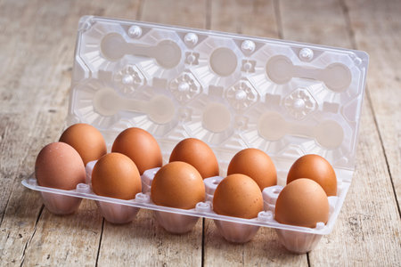Fresh chicken eggs on plastic container on rustic wooden table background.