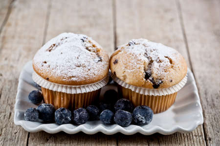 Homemade fresh muffins with sugar powder and blueberries on ceramic plate on rustic wooden table background.の写真素材