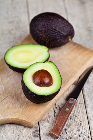 Avocado and knife on cutting board on old wooden table background. Fresh avocado halves on rustic wooden backround with copy space. Healthy food concept.の写真素材