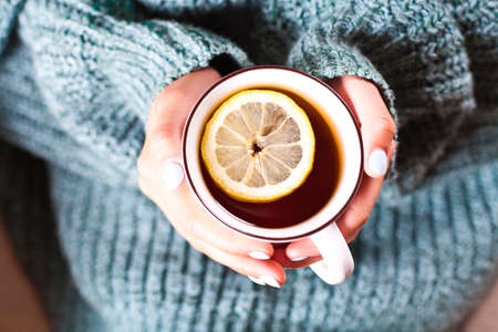 Female hands holding mug of hot tea with lemon in morning. Young woman relaxing tea cup on hand. Good morning tea or have a happy day message concept.の写真素材