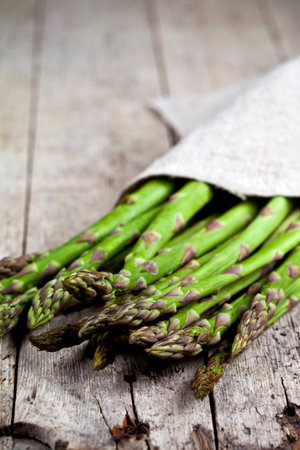 Bunch of fresh raw garden asparagus closeup and linen napkin on rustic wooden table background. Green spring vegetables. Edible sprouts of asparagus. With copy space.の写真素材