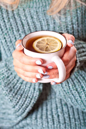 Female hands holding mug of hot tea with lemon in morning. Young woman relaxing tea cup on hand. Good morning tea or have a happy day message concept.の写真素材