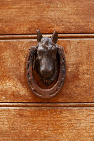 Ancient italian horse shaped door knocker on wooden brown door background.の写真素材