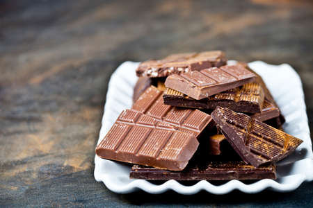 Chocolate bars pieces heap witn cinnamon powder on white ceramic plate. Sweet food photo concept. The chunks of broken chocolate stacked on black background with copy space.の写真素材