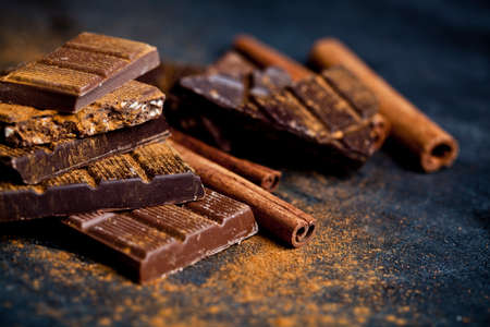 Chocolate stacked on black background. Chocolate bars pieces heap witn cinnamon powder and sticks. Sweet food photo concept with copy space.の写真素材