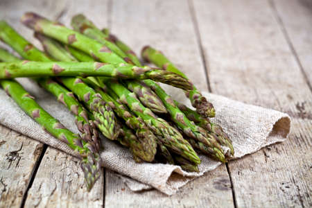 Bunch of fresh raw garden asparagus closeup and linen napkin on rustic wooden table background. Green spring vegetables. Edible sprouts of asparagus. With copy space.の写真素材